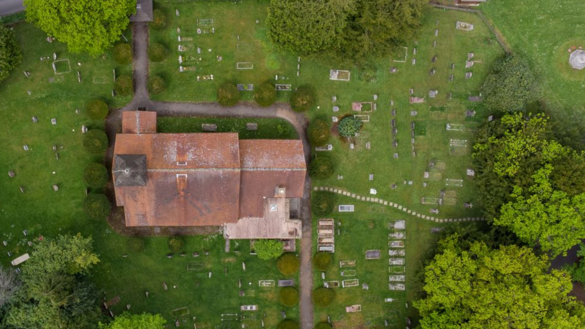 Top down view of a church roof surrounded by a churchyard, taken by a drone.