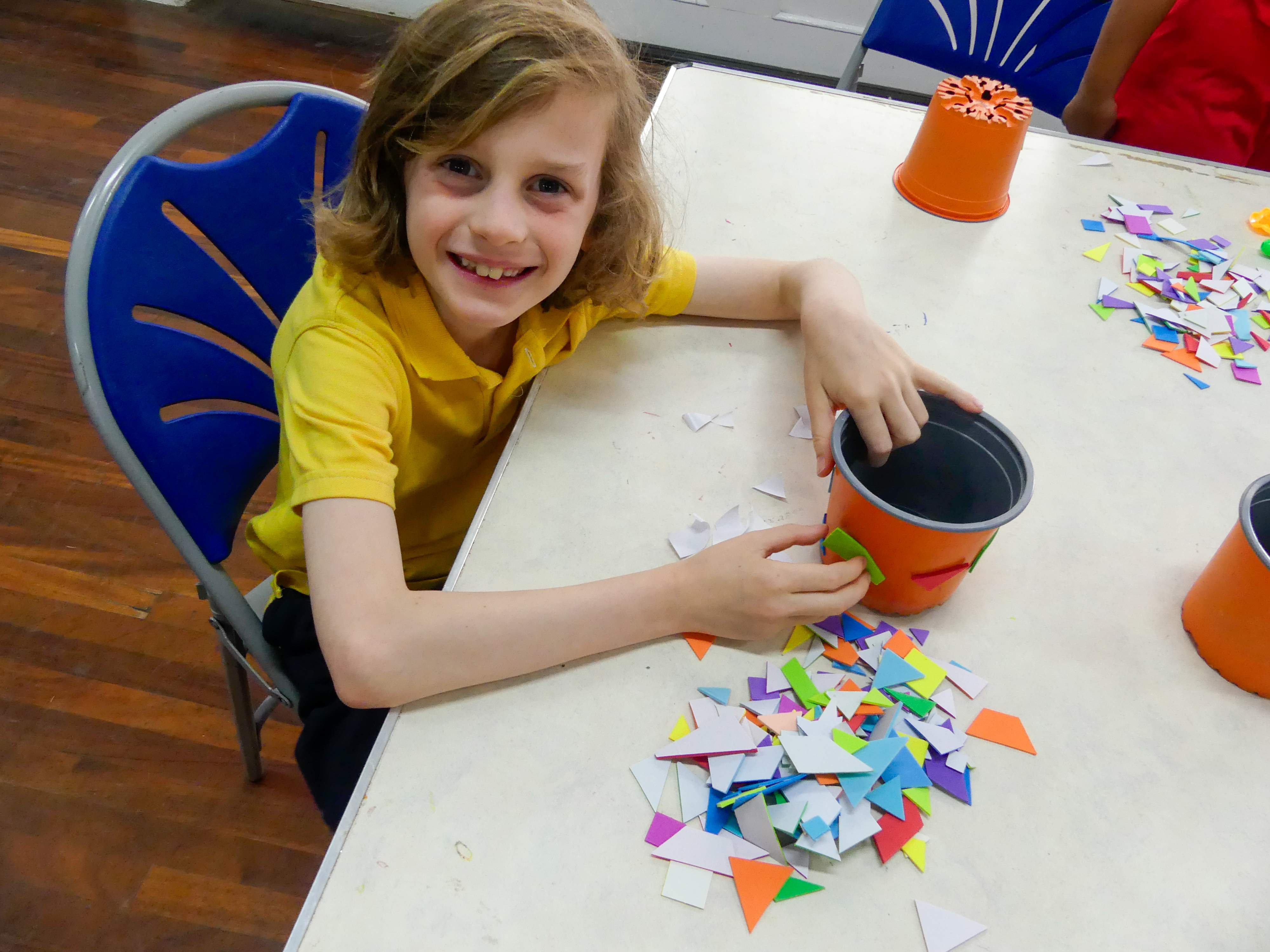 A young boy looks up and smiles as he sticks foam shapes on a plant pot