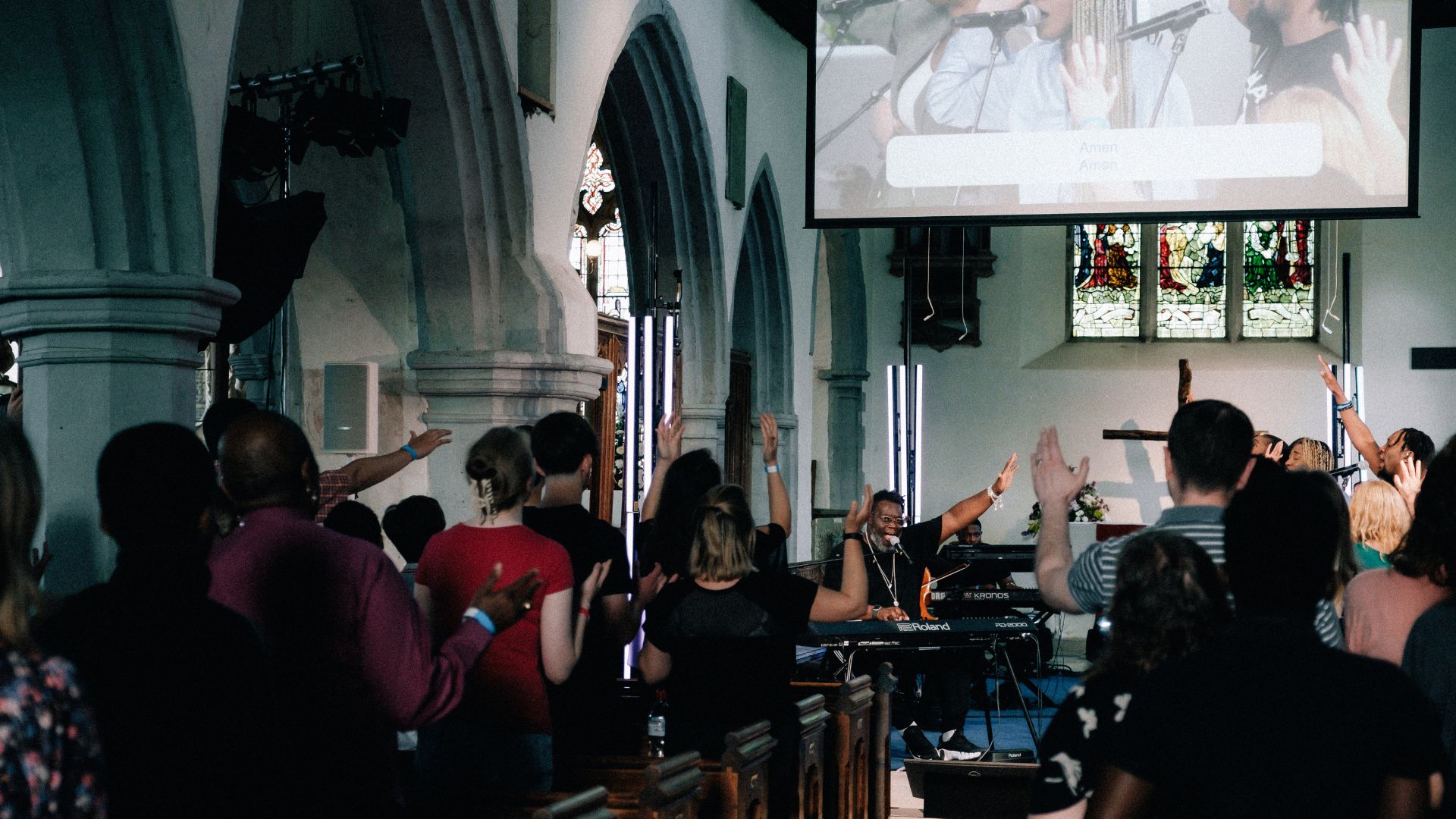 Young people wave their hands in the air as the worship band plays.