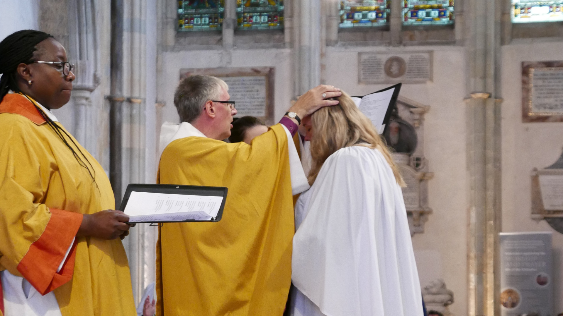 An ordinand stands in front of the bishop while he places his hands on her head.