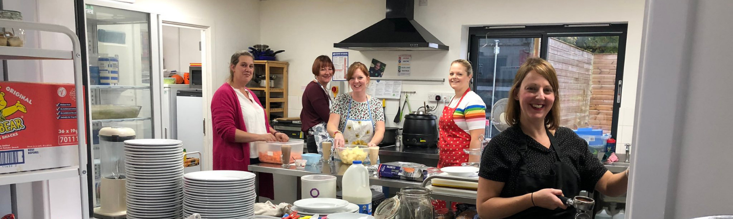 A group of women smile towards the camera as they prepare refreshments as part of a church cafe.