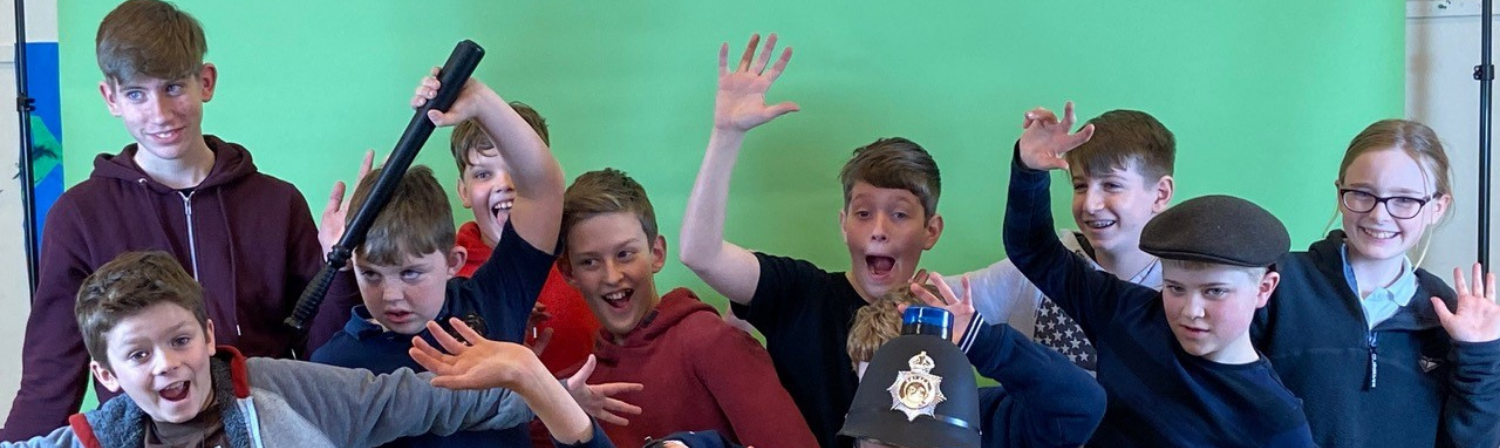 A group of young people make funny poses and raise their hands in the air in front of a 'green screen' as part of a film project funded by the Children and Young People Fund.