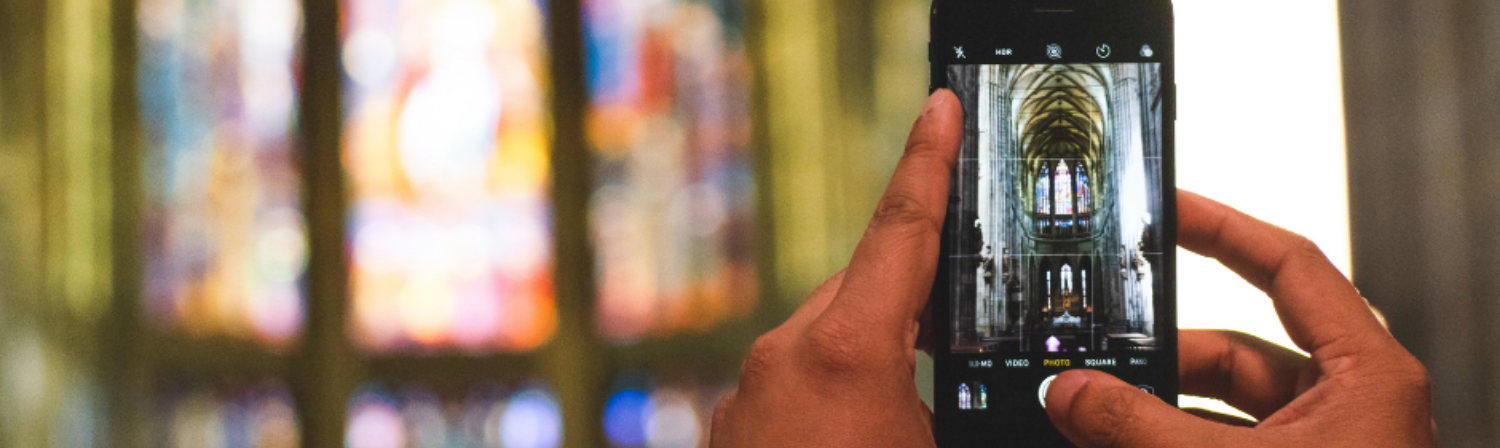 A phone is held up in a church as it takes a picture or video of a stained glass window.