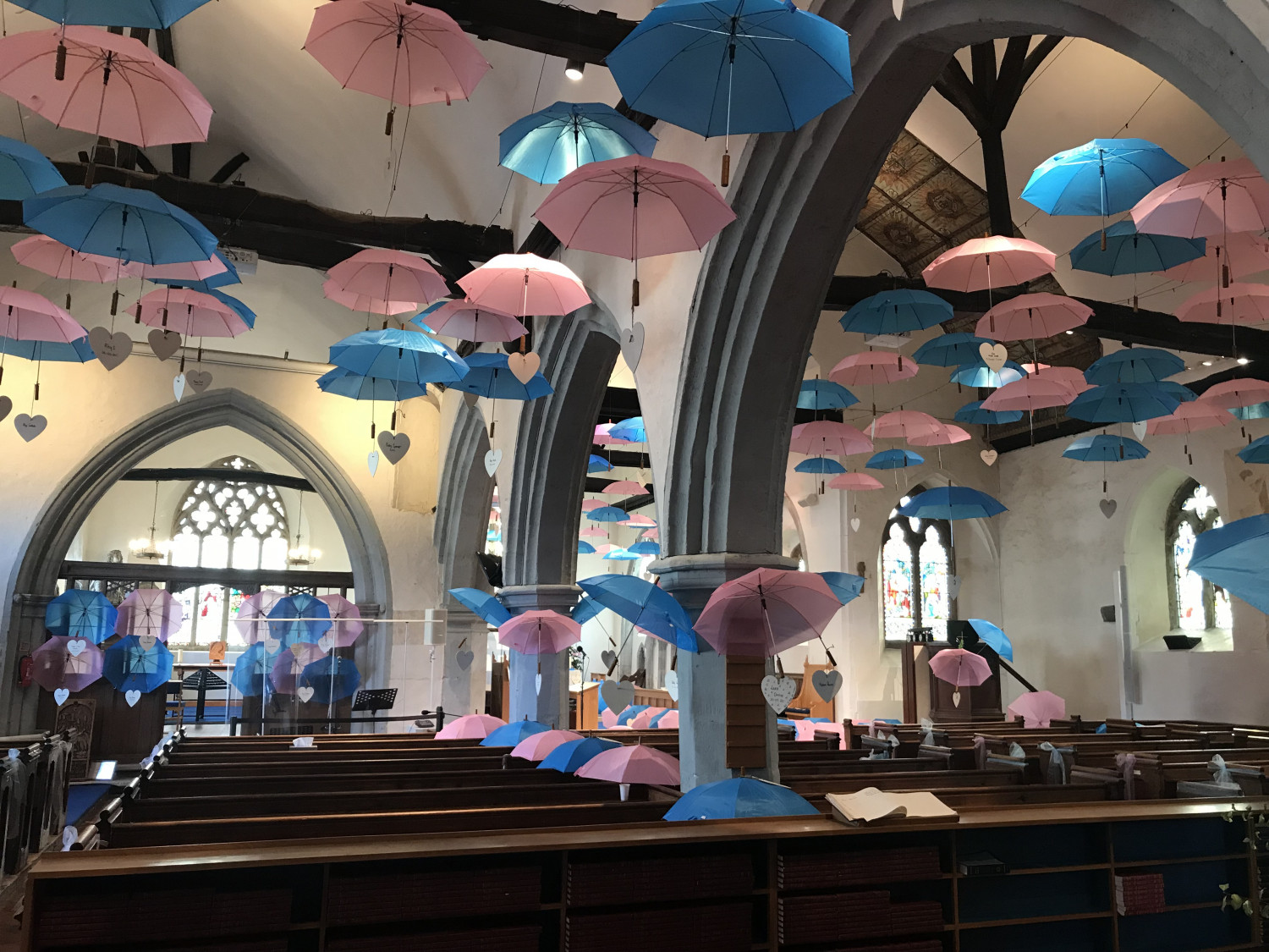 Hundreds of open pink and blue umbrellas hang from the ceiling of St Margaret's Church