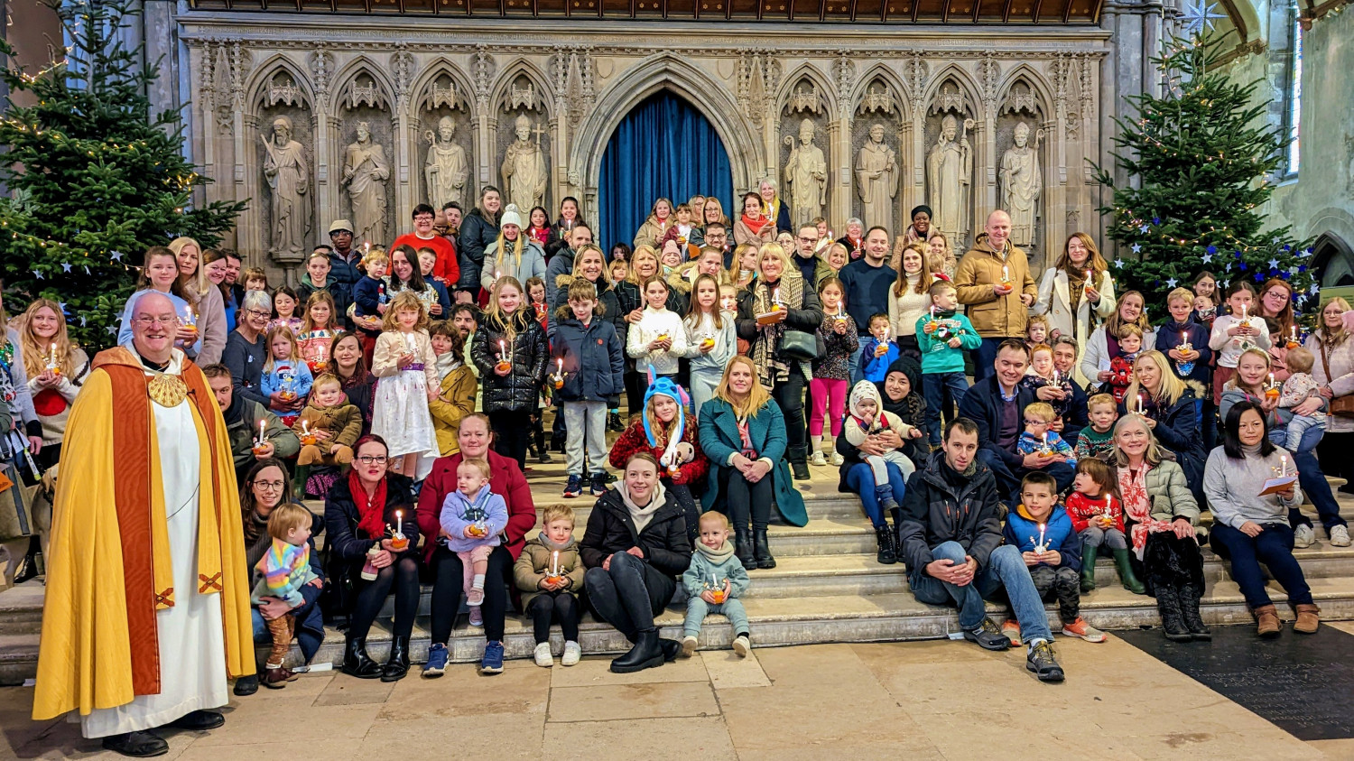 A mixed group of adults and children gather on the steps of the Nave altar with their christingles