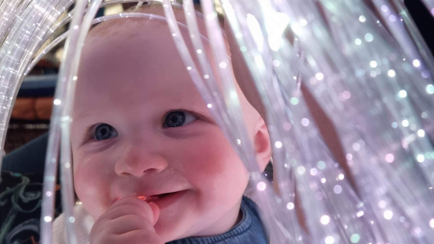 A small baby smiles as they enjoy sitting among a cascade of soft white lights.
