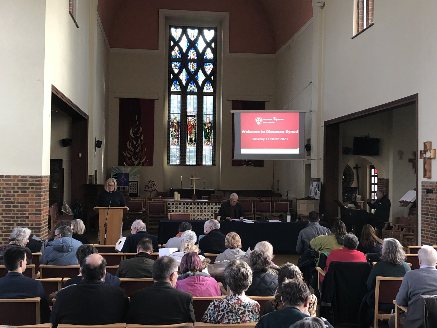 Back view of people sitting in a church. A screen shows a welcome sign